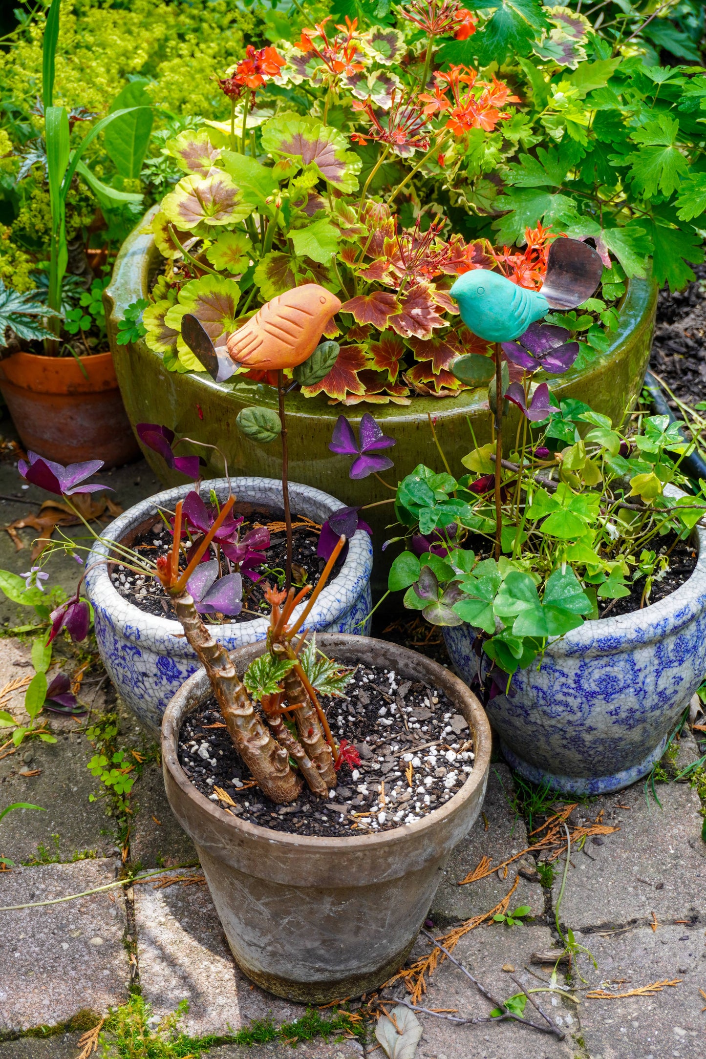 Potted plants with colorful flowers and small figurines on a stone path