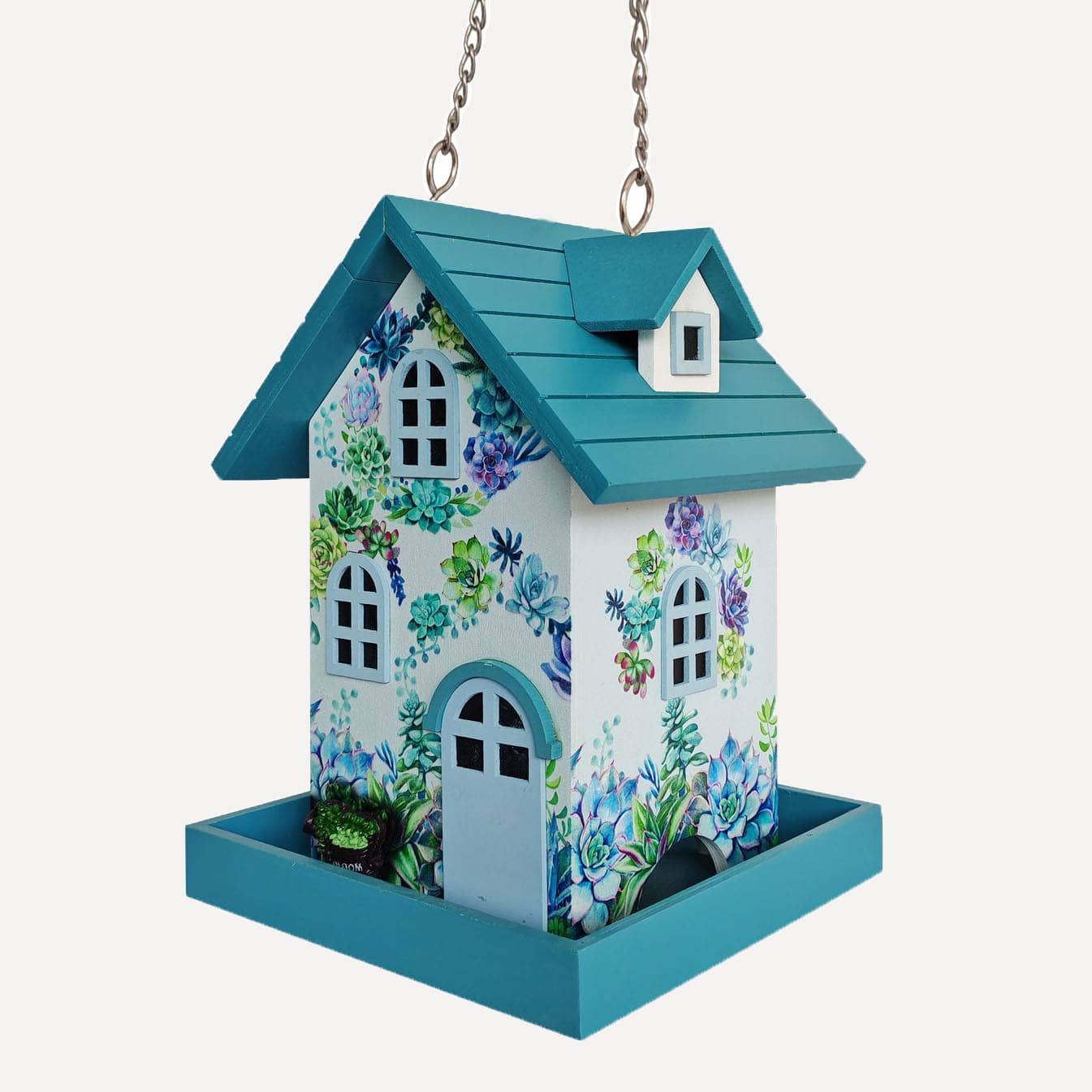 A hanging bird feeder with a teal roof and tray, decorated with a white front and sides covered in colorful floral and butterfly illustrations, suspended by metal chains against a light gray background.