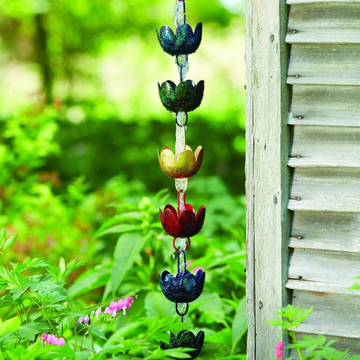 Colorful metal lotus flower cup rain chain hanging outdoors near wooden shutters and green foliage