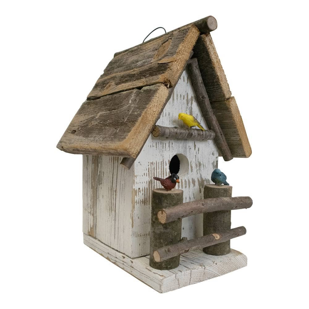A rustic birdhouse made from weathered wood, featuring a white-washed body, a slanted wooden roof with a hanging loop, a small round entrance hole, a perch, and two log-style supports. Three small decorative birds are perched on the structure: one yellow, one reddish-brown, and one blue-gray.
