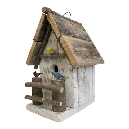 A rustic wooden birdhouse with a weathered white and brown painted finish, featuring a slanted roof, small log-style perches, and three small decorative birds perched on the front.