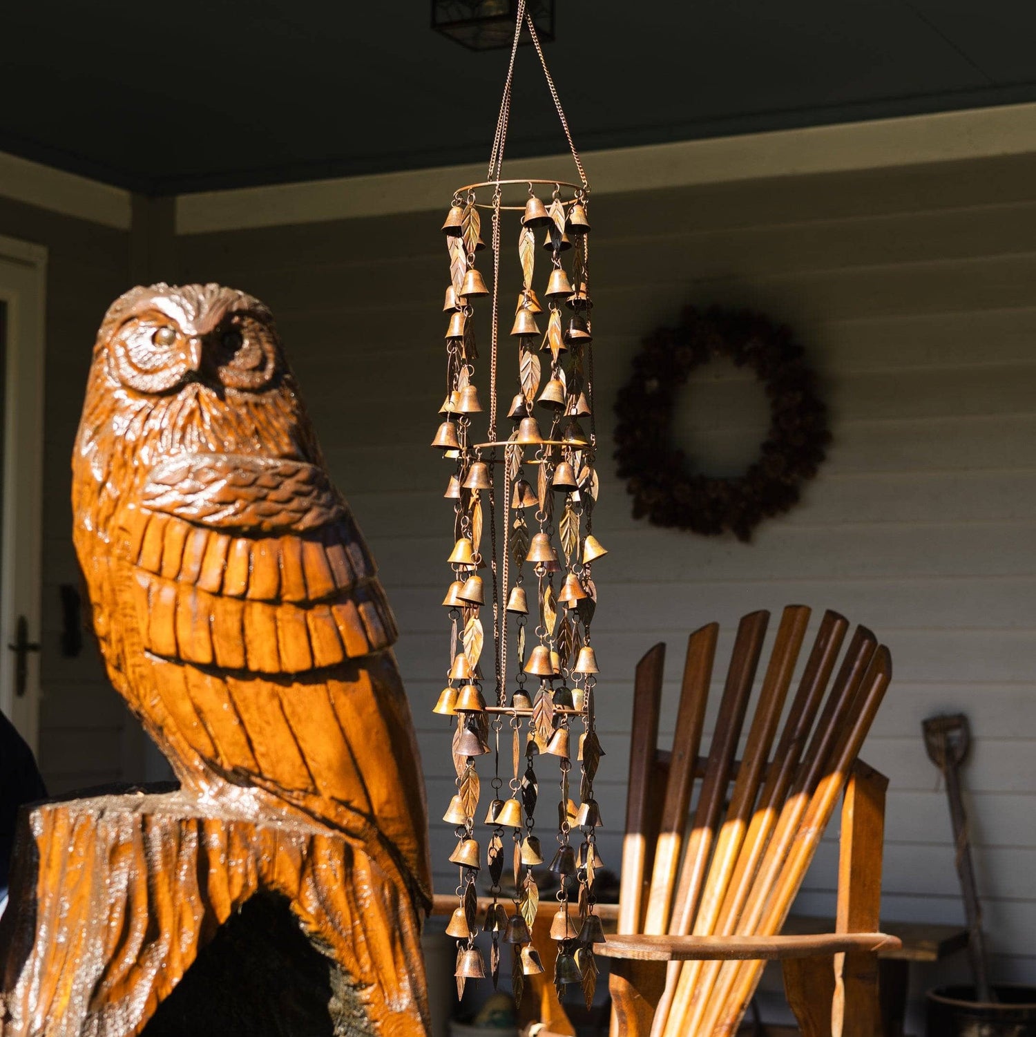 Copper-toned metal wind chime with triple tiers of small bells and leaf accents hanging on a porch