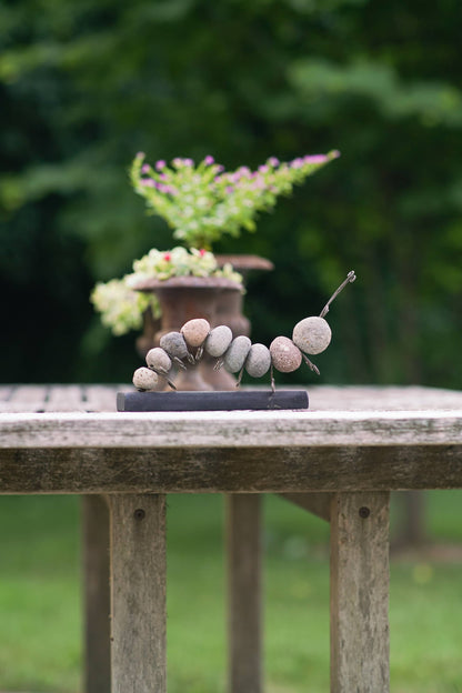 Handmade stone caterpillar sculpture with wire legs and antennae mounted on a dark rectangular base