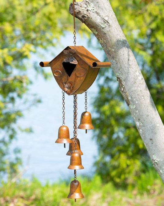 Copper-toned metal birdhouse wind chime with butterfly cutout and five hanging bells, suspended from a tree branch