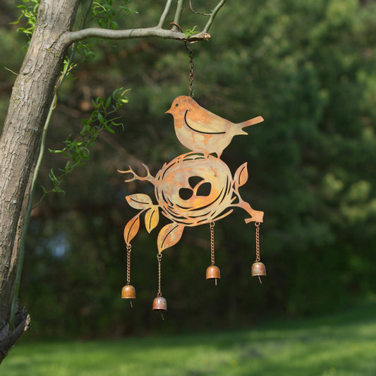 Rusty metal wind chime with cutout bird perched on a nest with eggs, hanging from a tree branch with four small copper bells