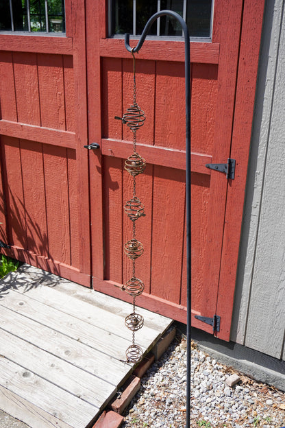 Copper-toned metal spiral ring wind chime with a ball centre, hanging on a chain against a green background