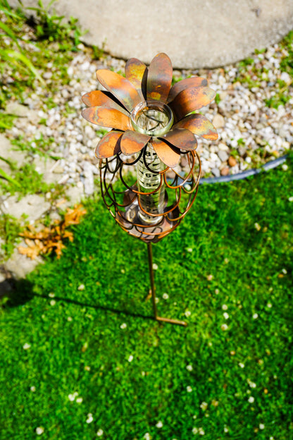 Rusty copper metal pineapple-shaped rain gauge garden stake with glass tube and measurement markings, placed on grass