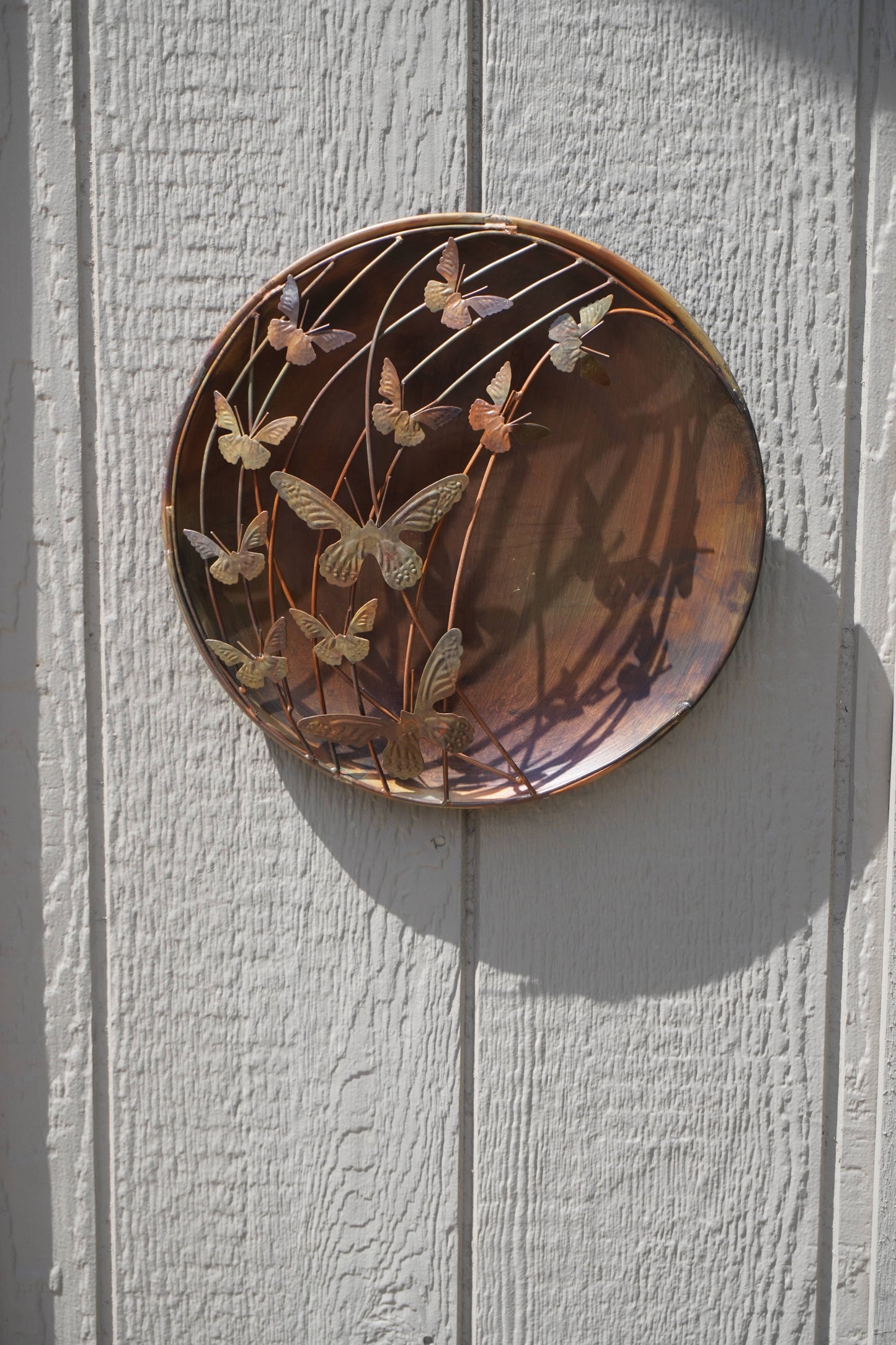 Decorative metal plate with butterfly design on a white wall