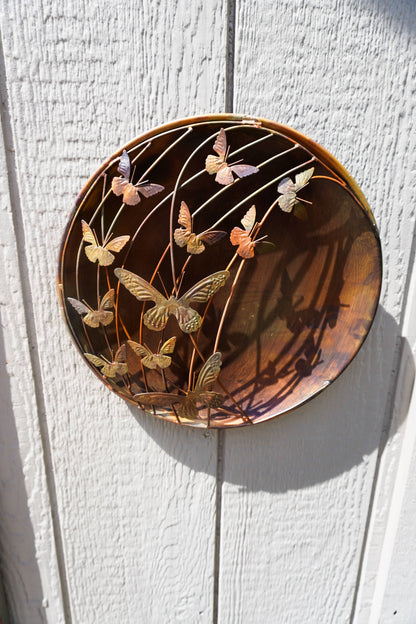 Decorative metal wall art with butterfly design on a wooden surface