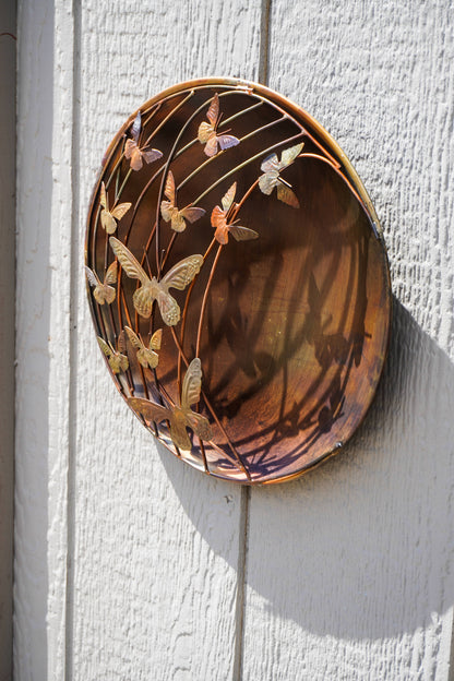 Decorative metal plate with butterfly design on a white wooden surface