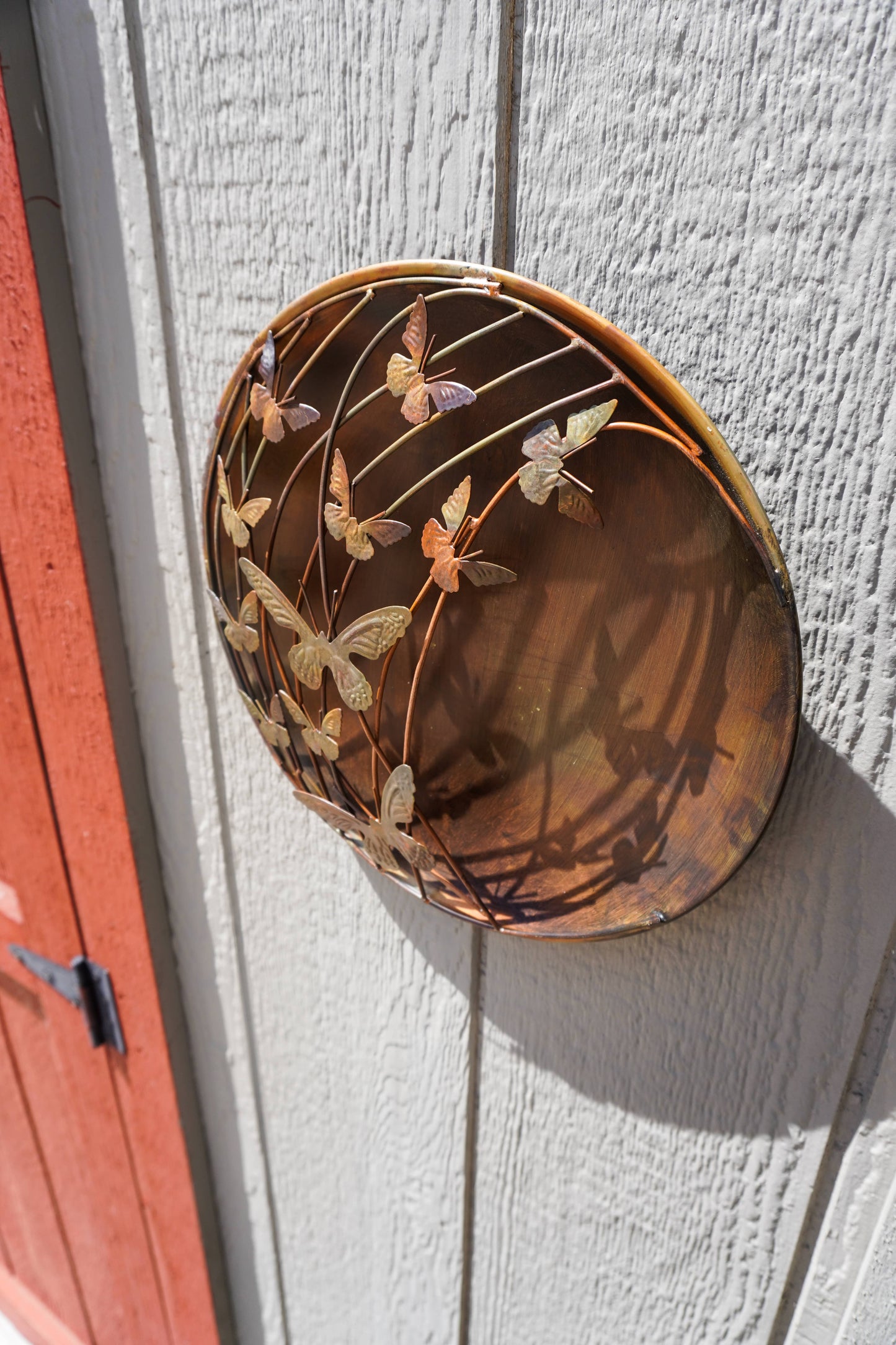 Decorative metal wall art with butterfly design on a light gray wall.