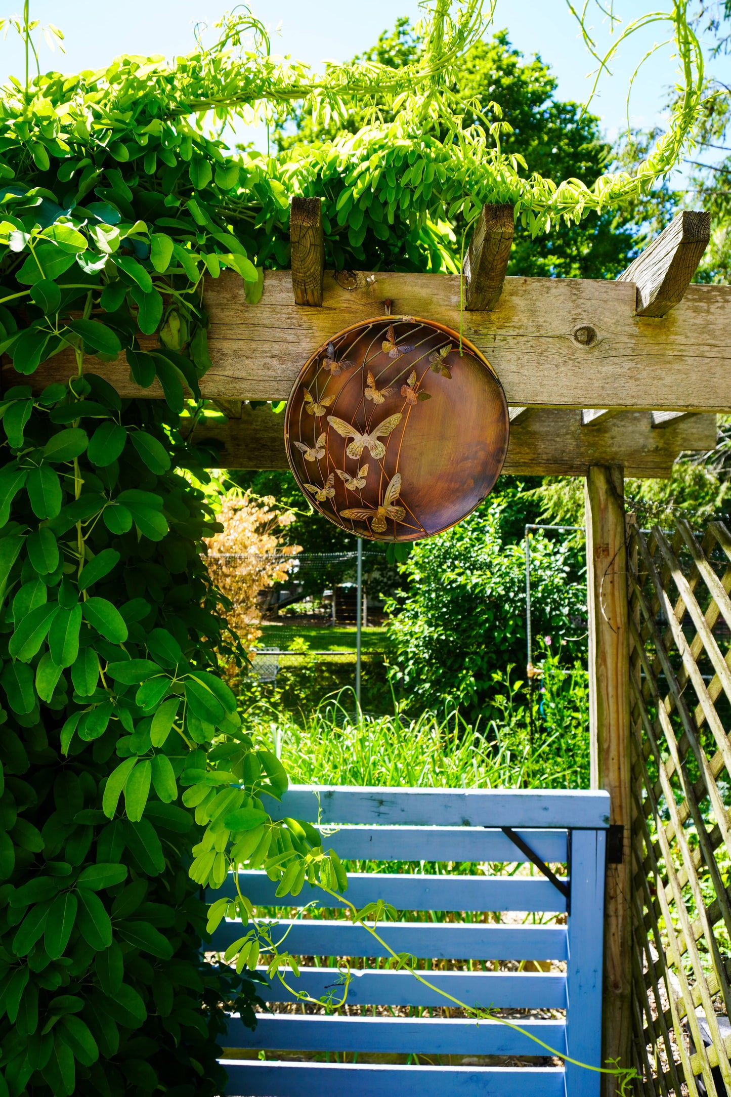 Decorative metal plate with butterfly design on a wooden pergola with green foliage.