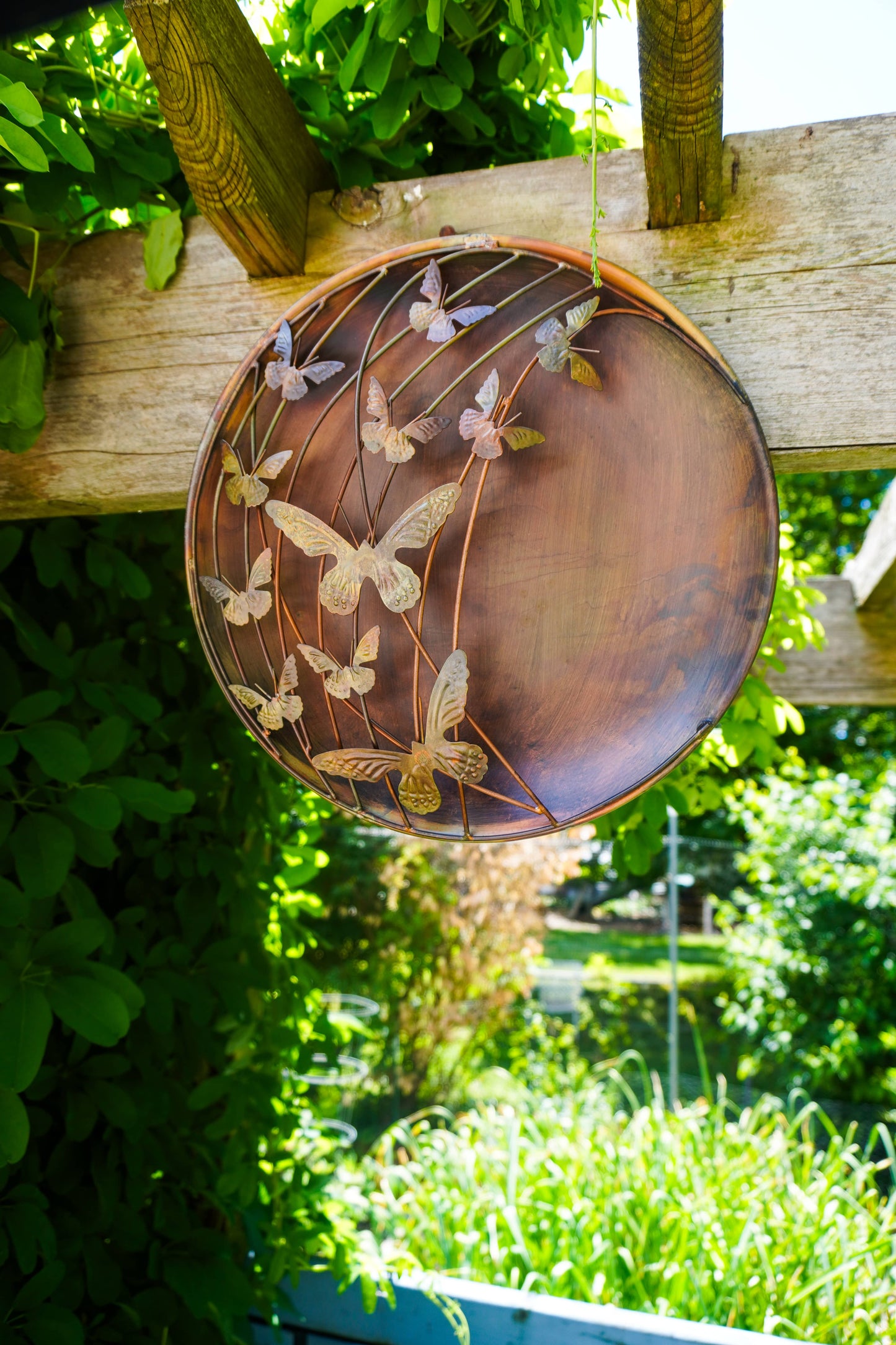 Decorative metal plate with butterfly design hanging on a wooden fence with a garden background