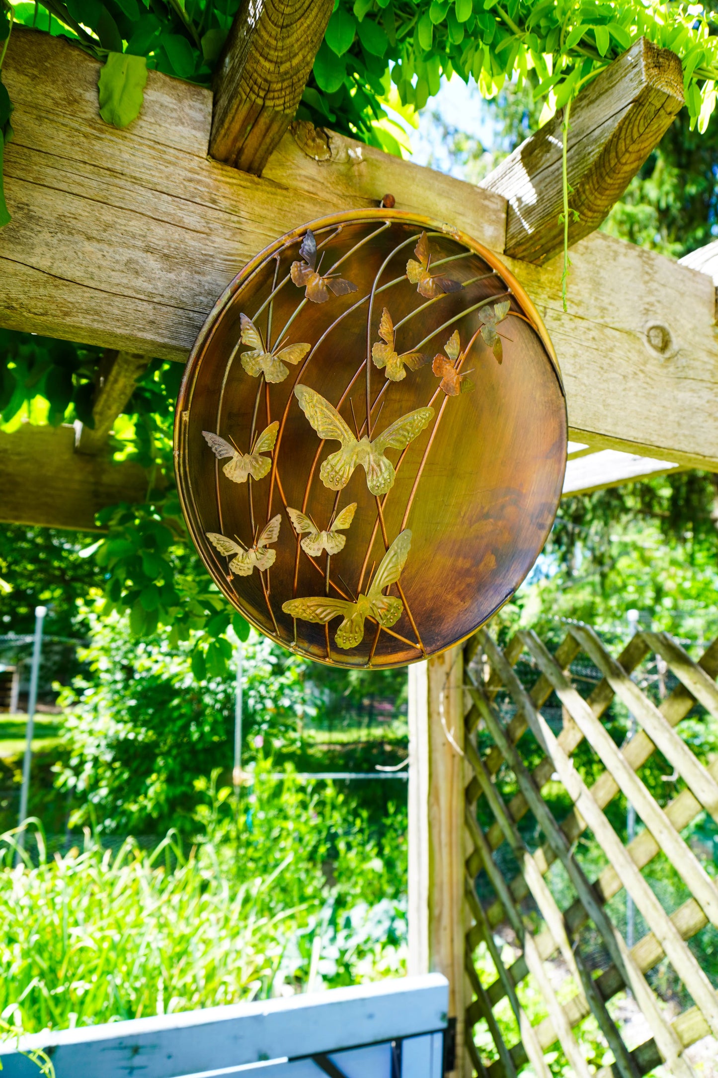 Decorative metal butterfly wall art on a wooden post with a garden background