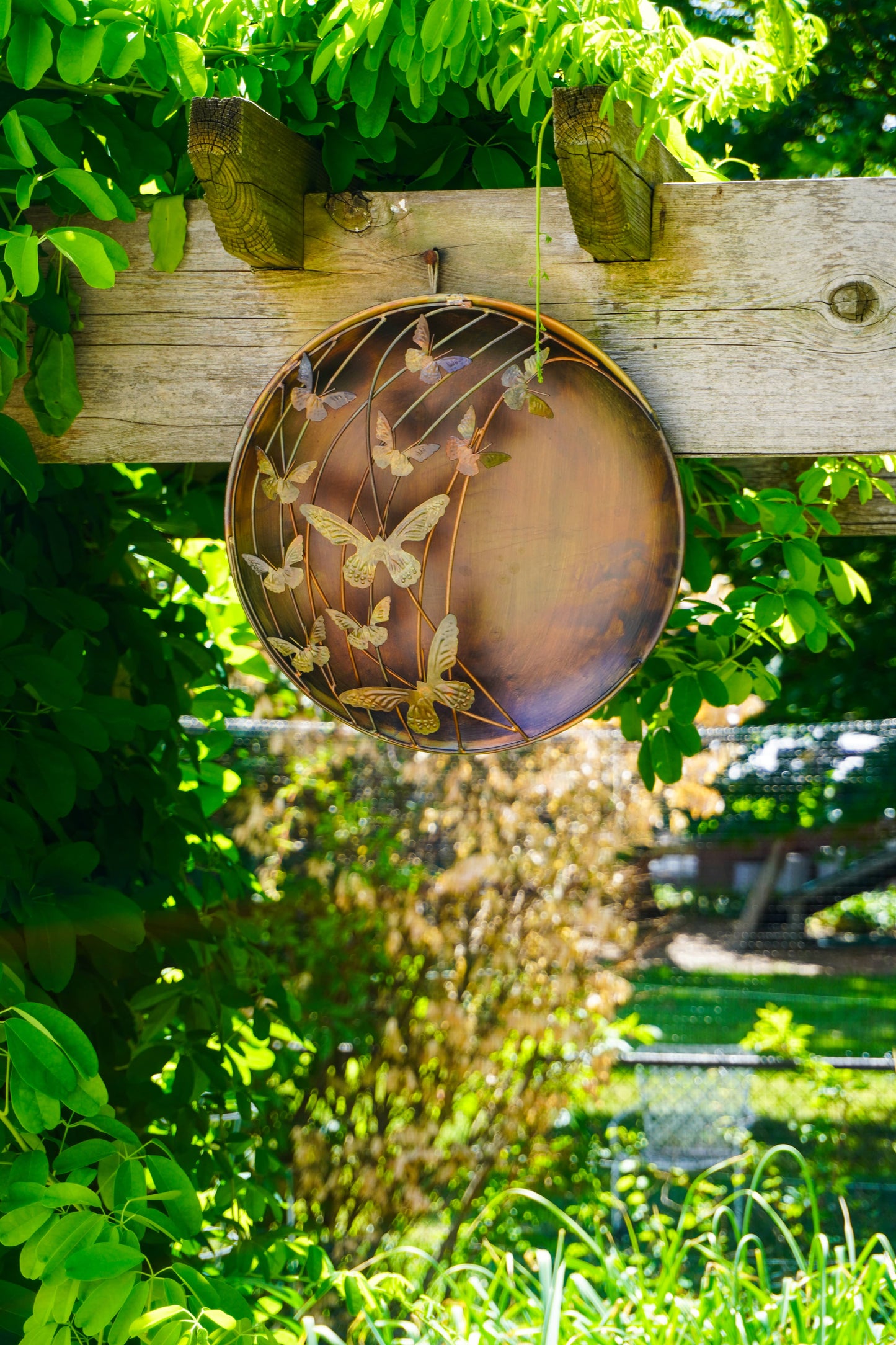 Decorative metal plate with butterfly design on a wooden post surrounded by green foliage