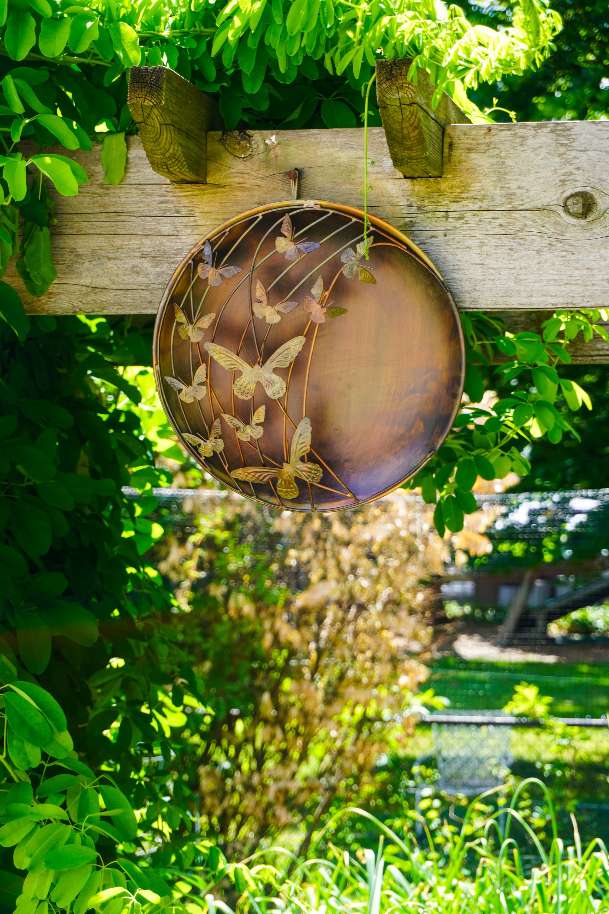 Decorative metal plate with butterfly design on a wooden post surrounded by green foliage