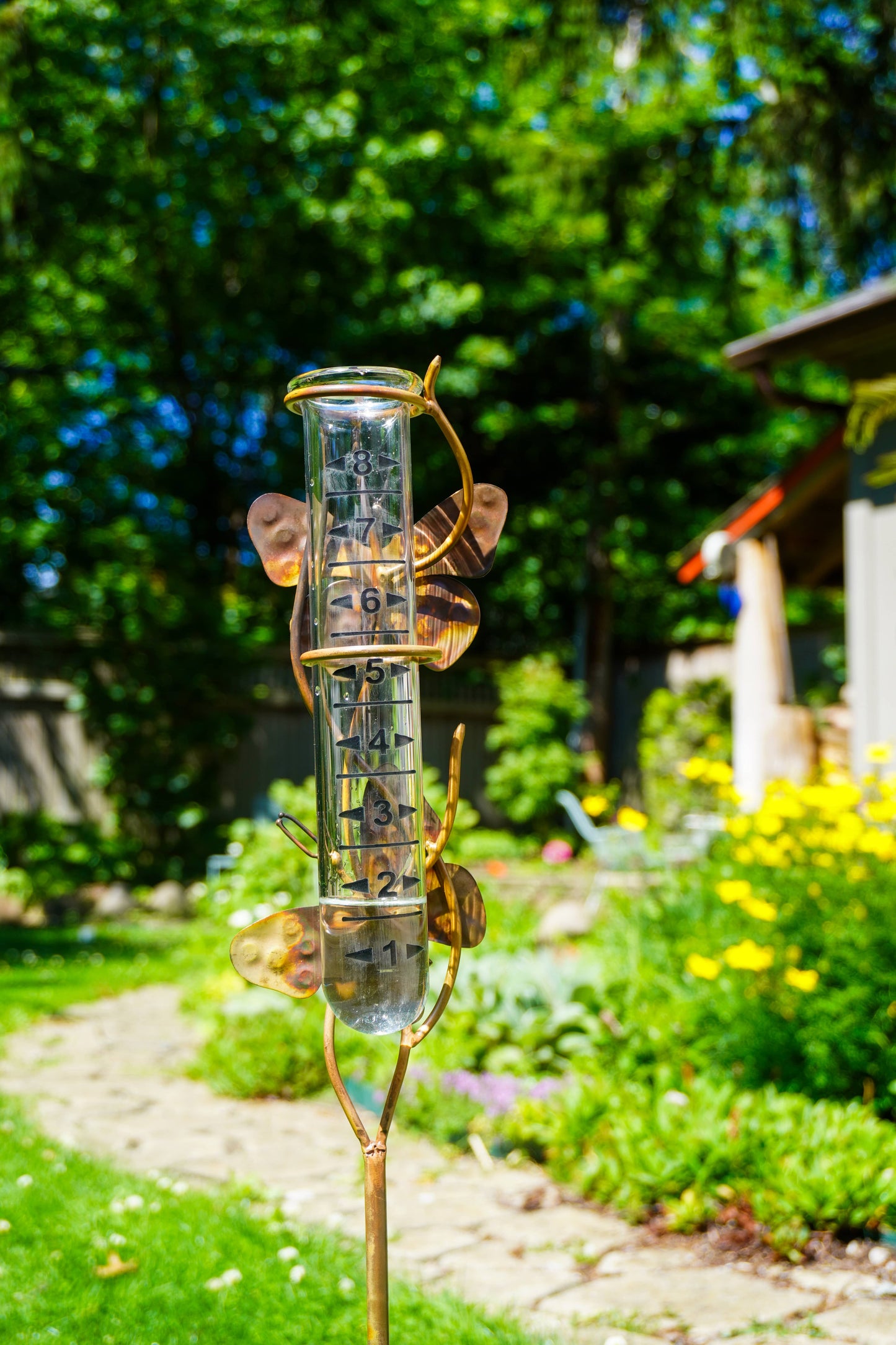 Rain gauge in a garden with greenery and flowers in the background