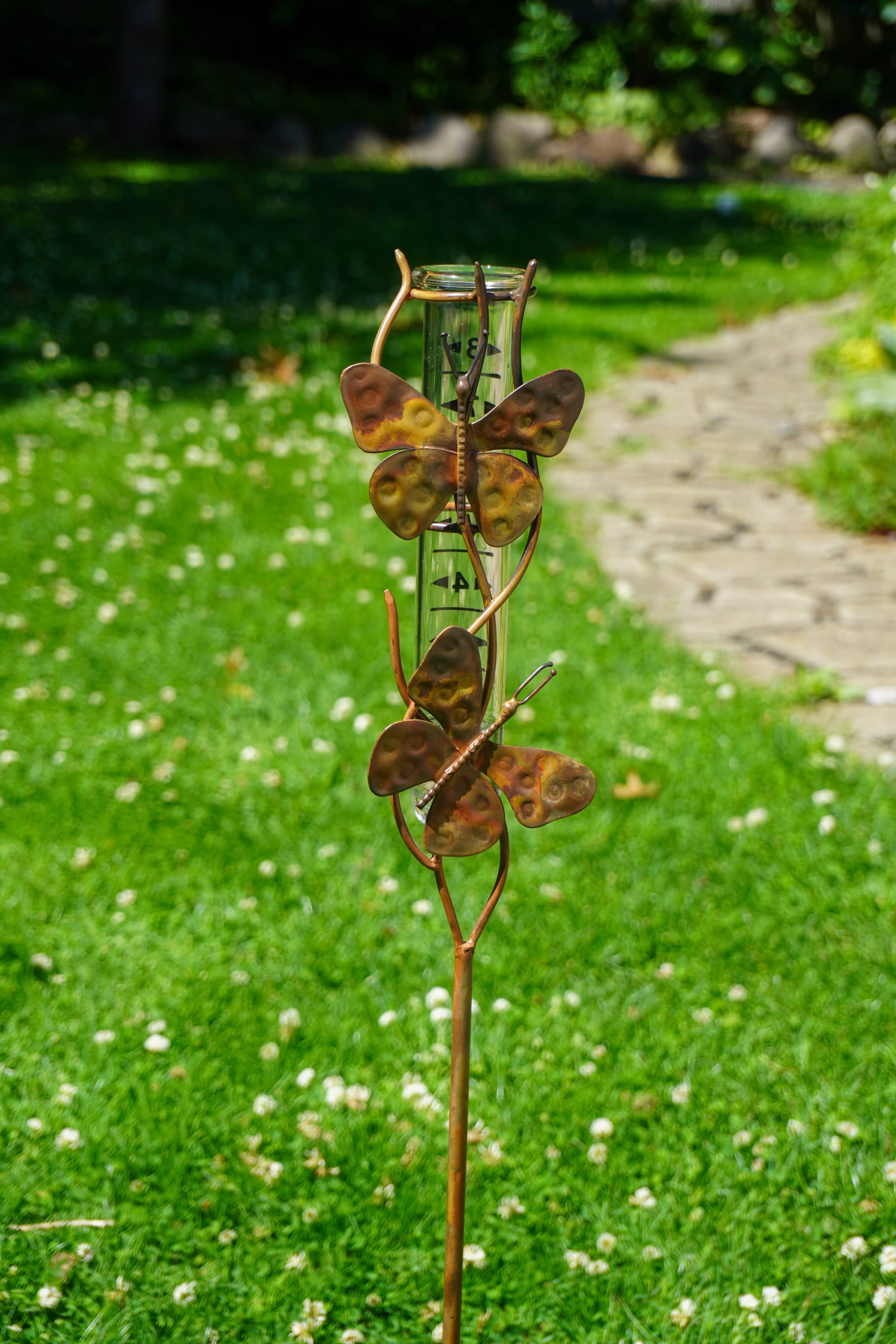 Butterfly-themed rain gauge in a garden setting