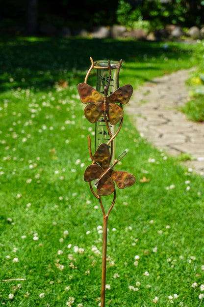 Butterfly-themed rain gauge in a garden setting