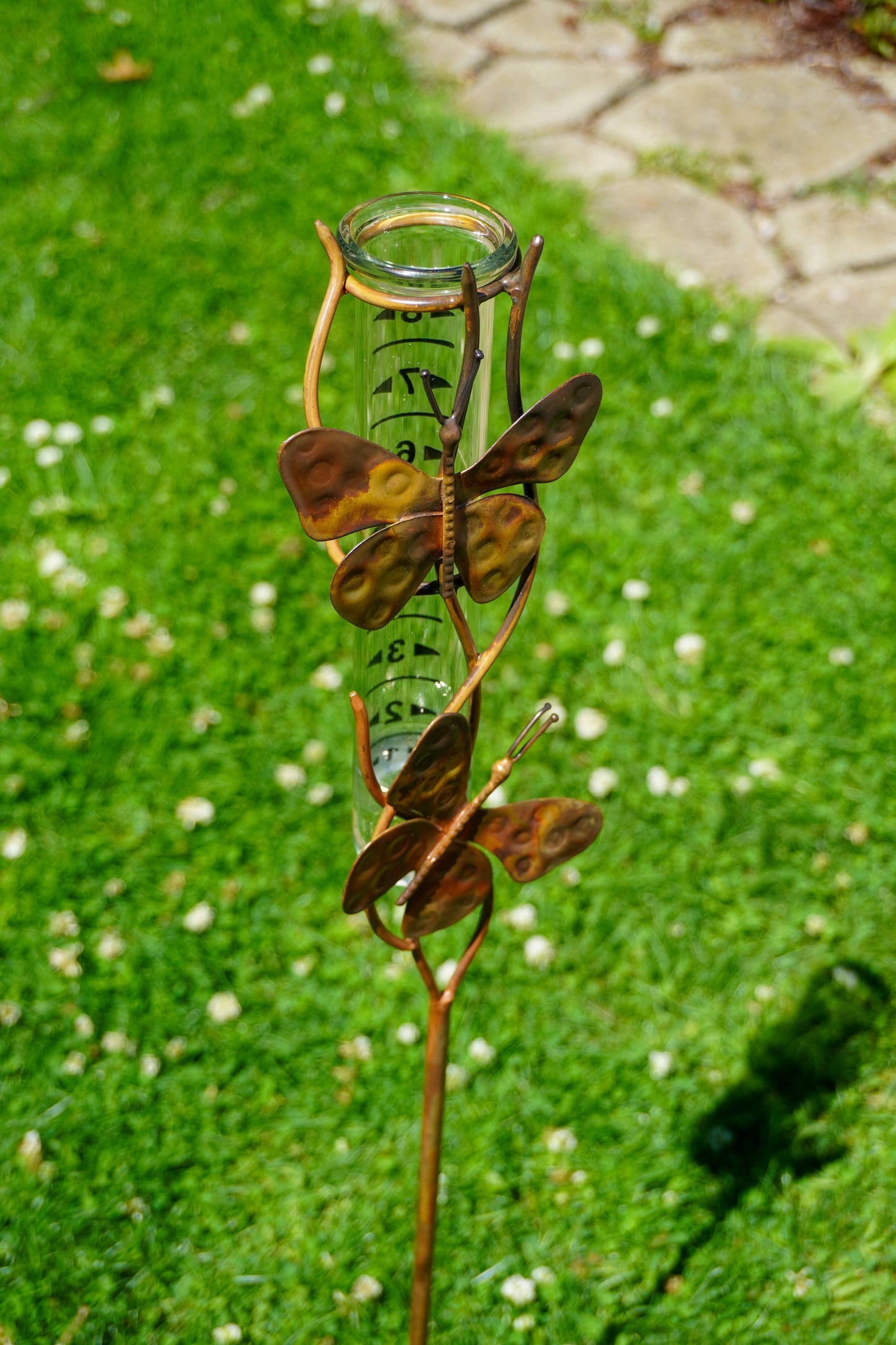 Decorative metal butterfly sculpture with a glass container on a green grass background