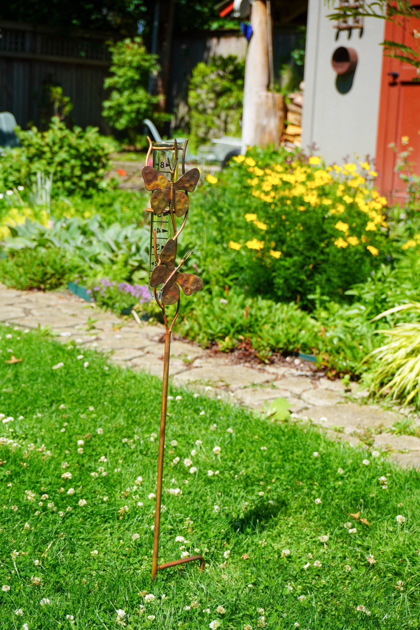 Metal butterfly sculpture on a garden path with flowers and plants in the background