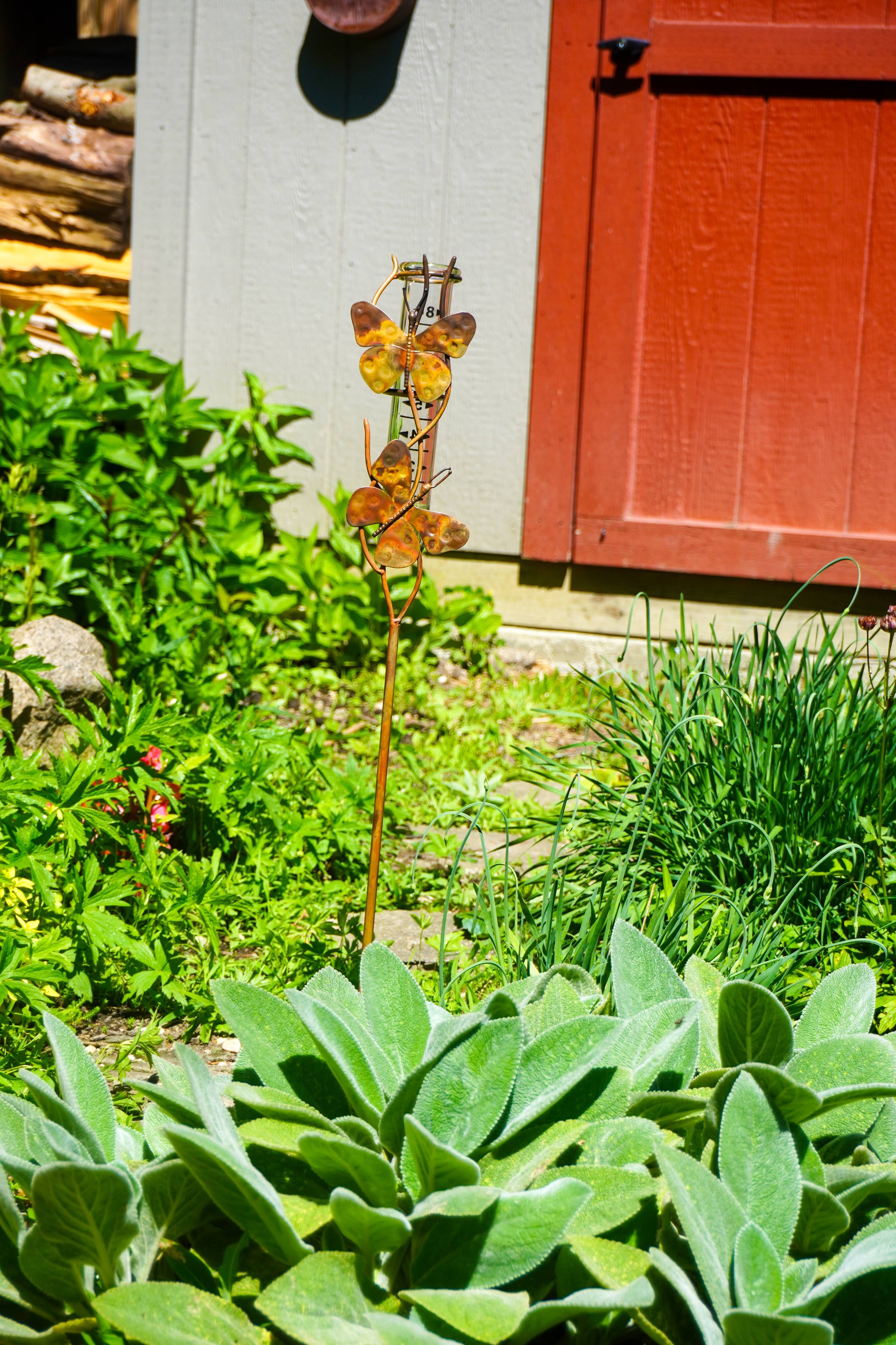 Garden scene with butterfly-shaped metal sculpture and green plants in front of a red door.