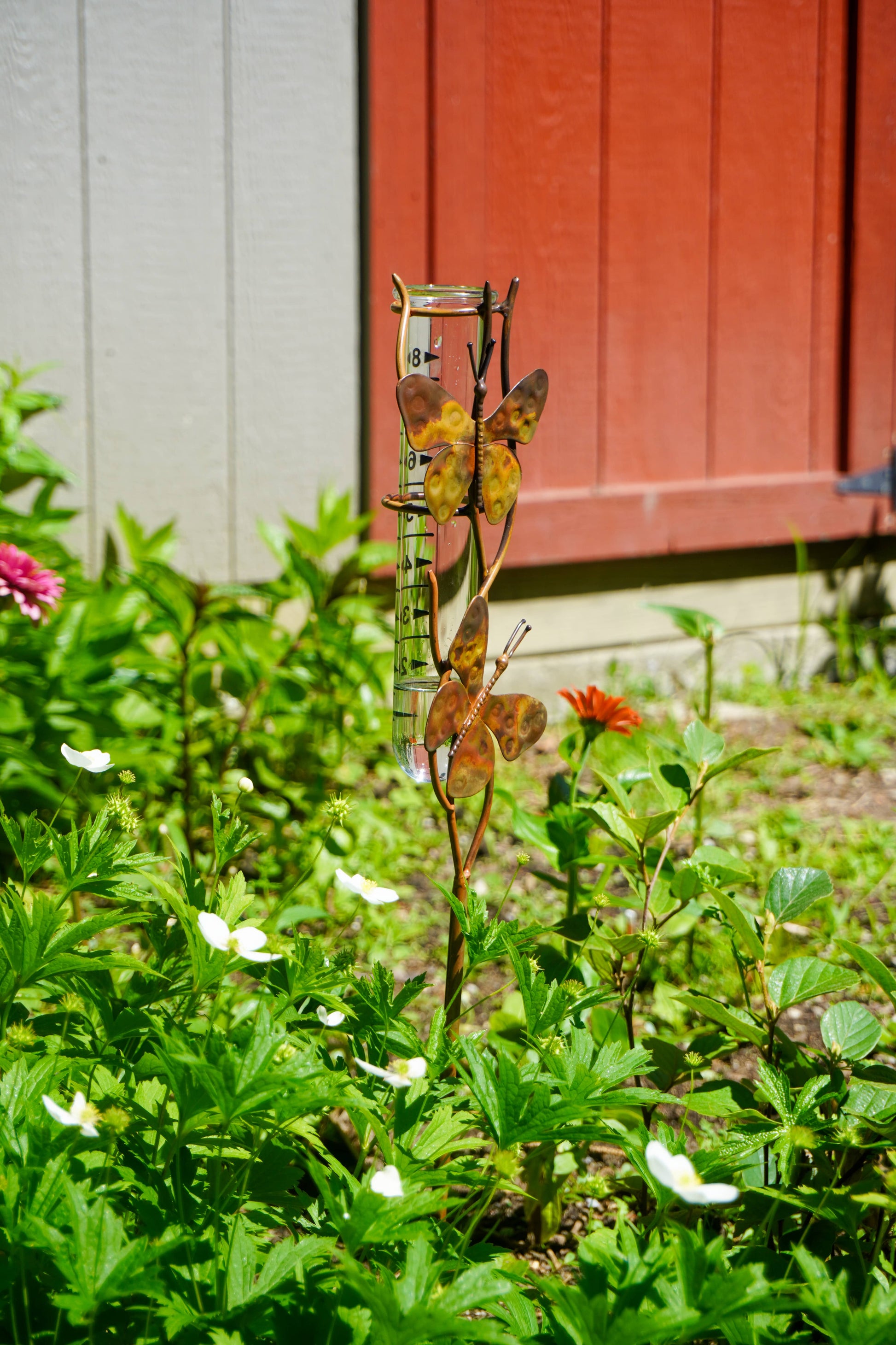 Metallic butterfly garden ornament in a garden with flowers and a red wooden door in the background.