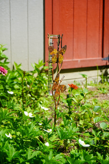 Metallic butterfly garden ornament in a garden with flowers and a red wooden door in the background.