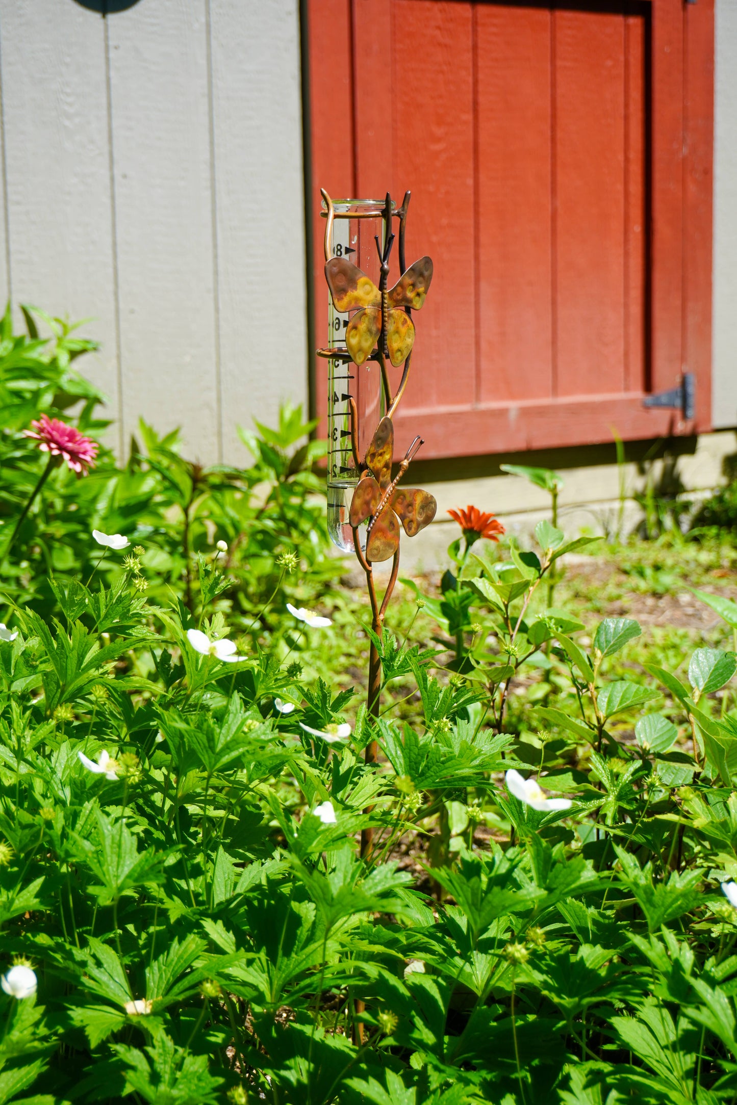 Metallic butterfly sculpture in a garden with flowers and a red door in the background