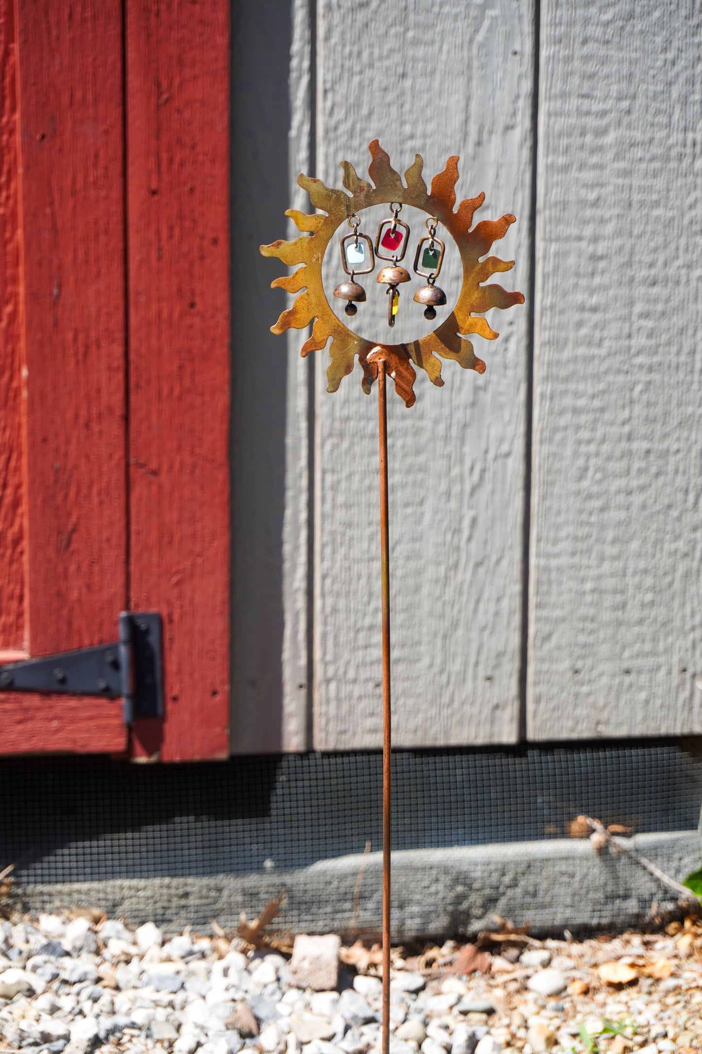 Decorative sun-shaped garden stake with face design against a red and gray wooden background.