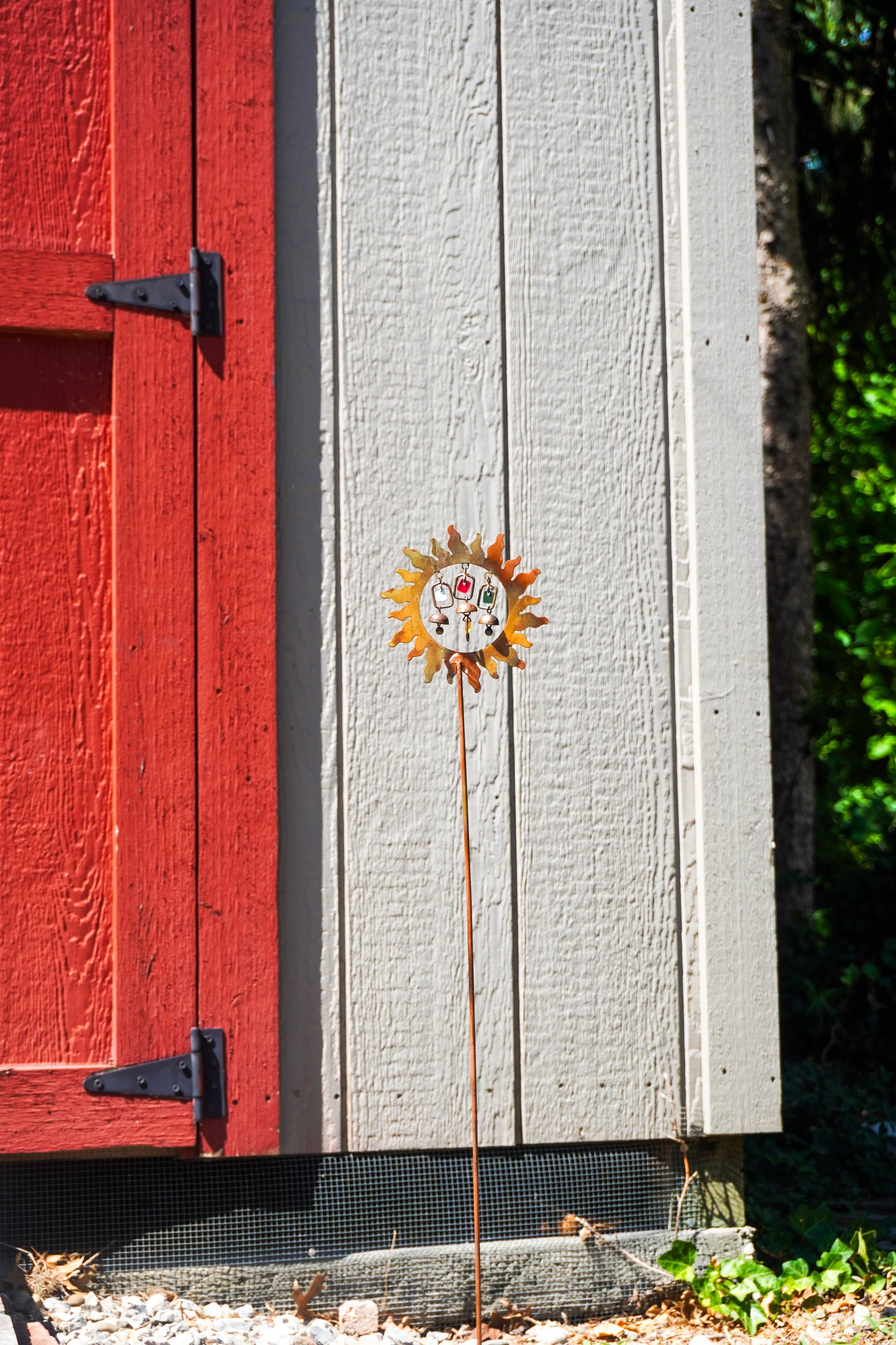Decorative metal sun garden stake in front of a wooden barn with a red door.