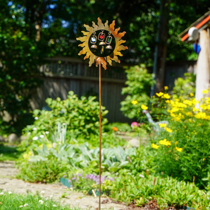 Decorative sun-shaped garden stake in a lush garden setting with trees and flowers.