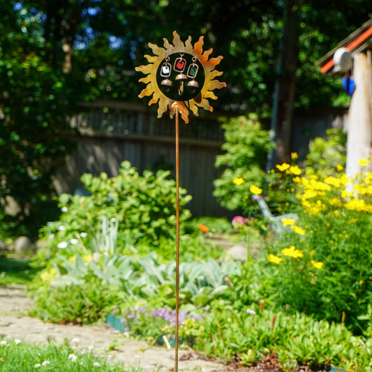 Decorative sun-shaped garden stake in a lush garden setting with trees and flowers.