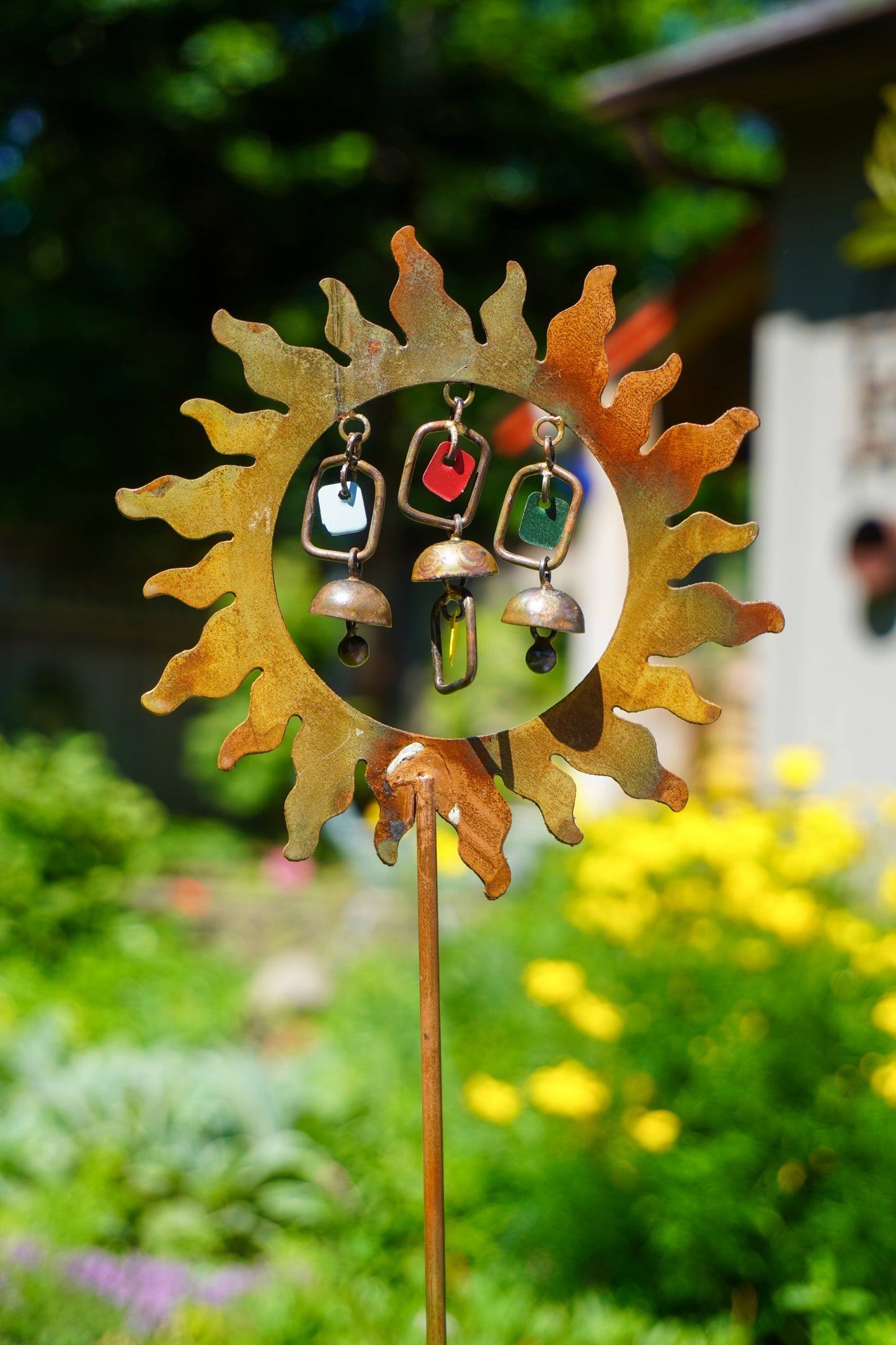 Decorative garden stake with sun design and hanging bells in a garden setting