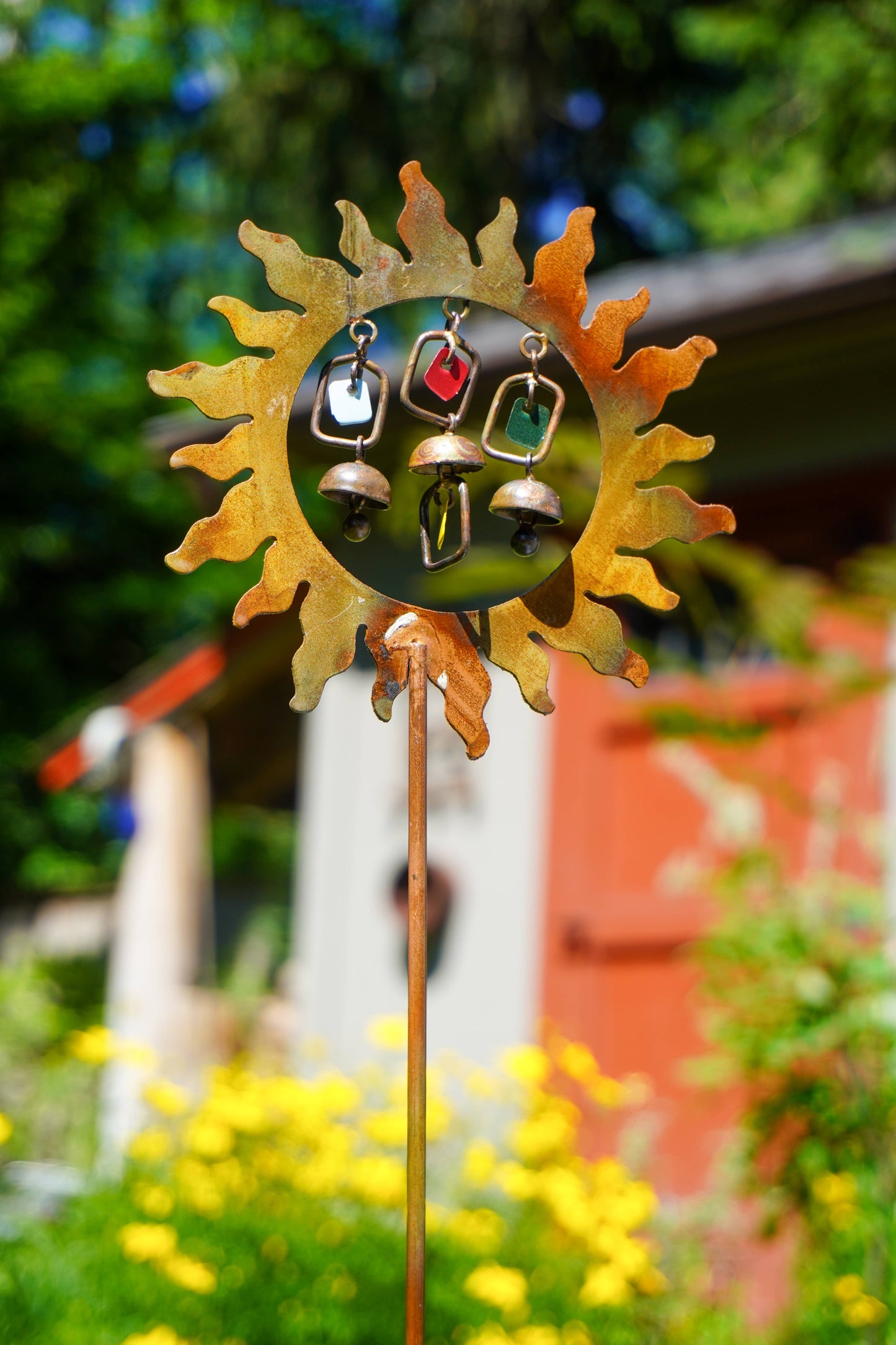 Decorative sun-shaped garden stake with hanging bells in a garden setting