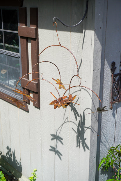 A metal dragonfly wall hanging suspended outdoors against a white house exterior wall, with its shadow cast on the wall.