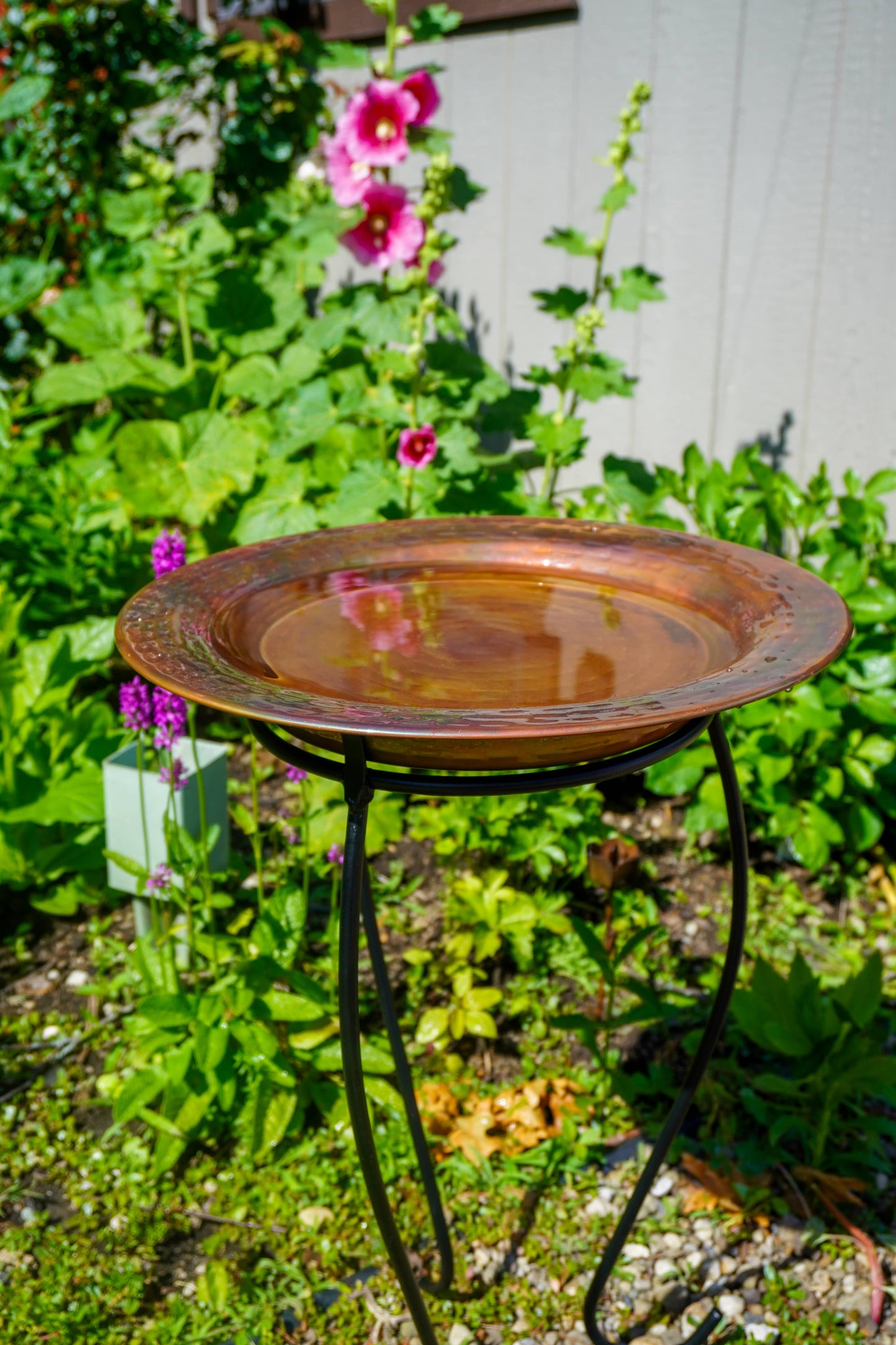 Hammered copper round birdbath with iridescent finish on curved metal stand.