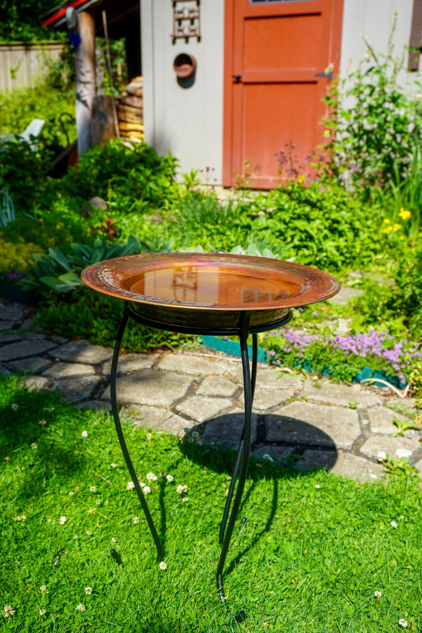 Hammered copper round birdbath with iridescent finish on curved metal stand.
