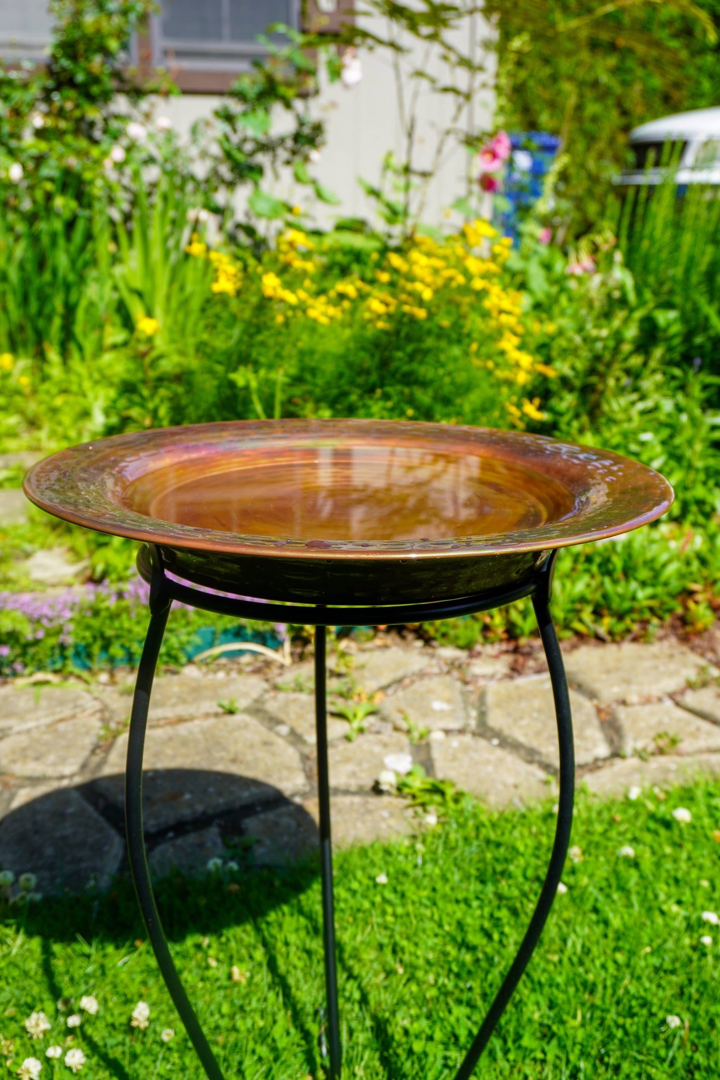 Hammered copper round birdbath with iridescent finish on curved metal stand.