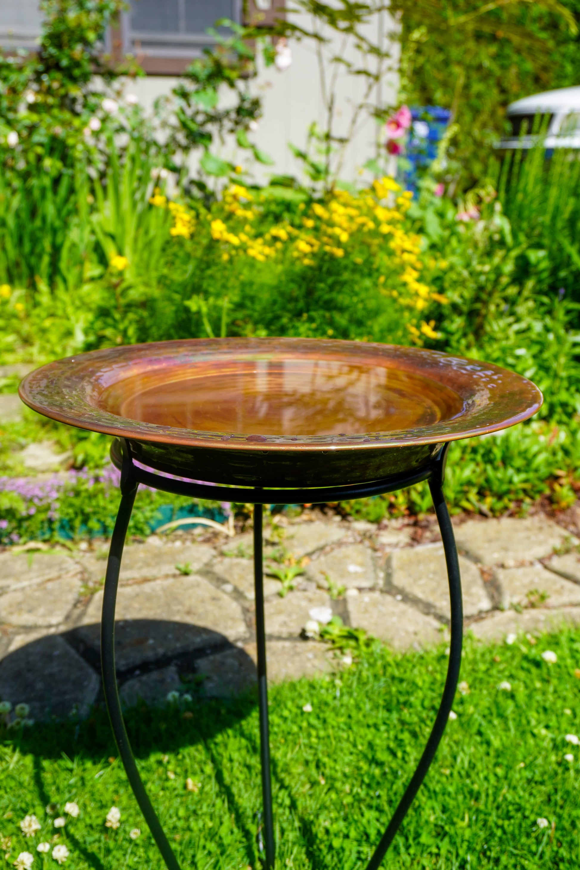 Hammered copper round birdbath with iridescent finish on curved metal stand.