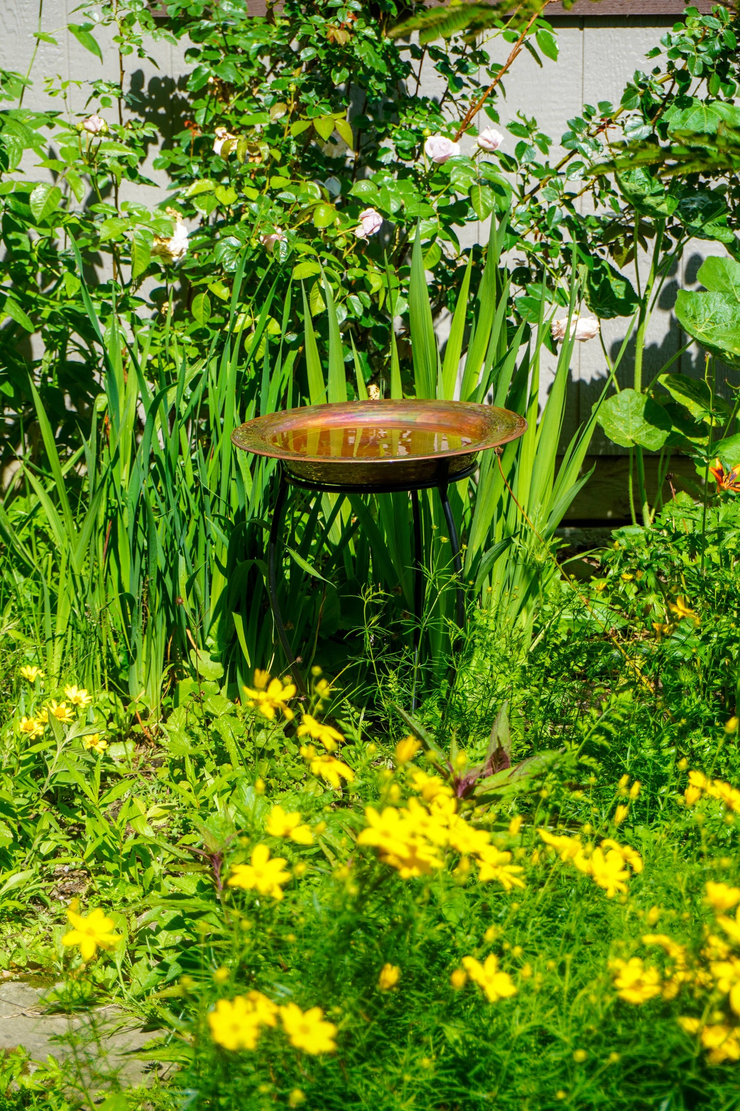 Hammered copper round birdbath with iridescent finish on curved metal stand.