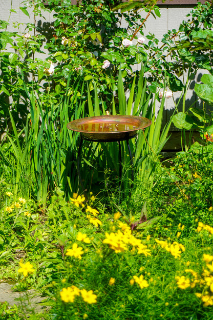 Hammered copper round birdbath with iridescent finish on curved metal stand.