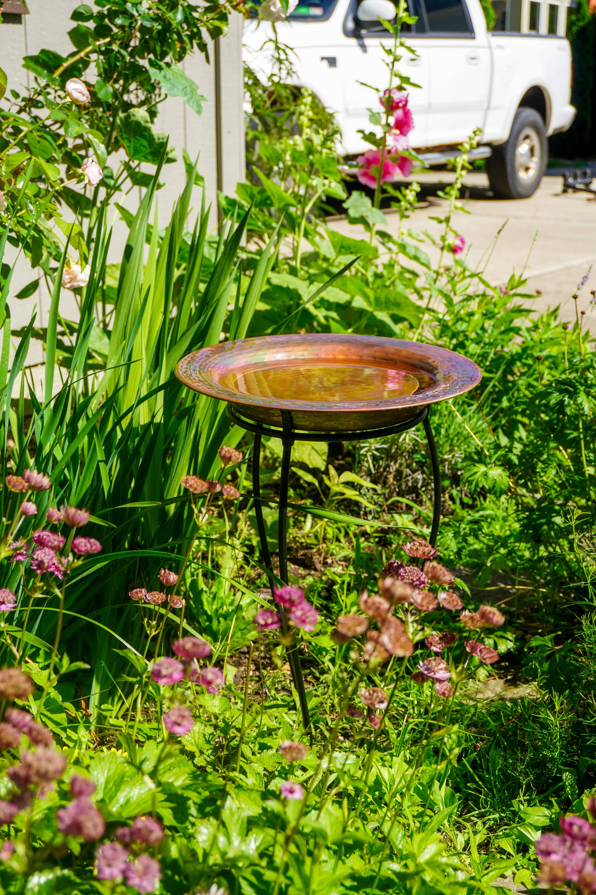 Hammered copper round birdbath with iridescent finish on curved metal stand.