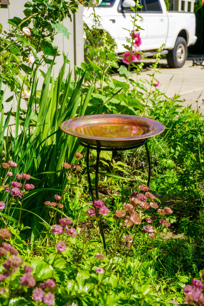Hammered copper round birdbath with iridescent finish on curved metal stand.