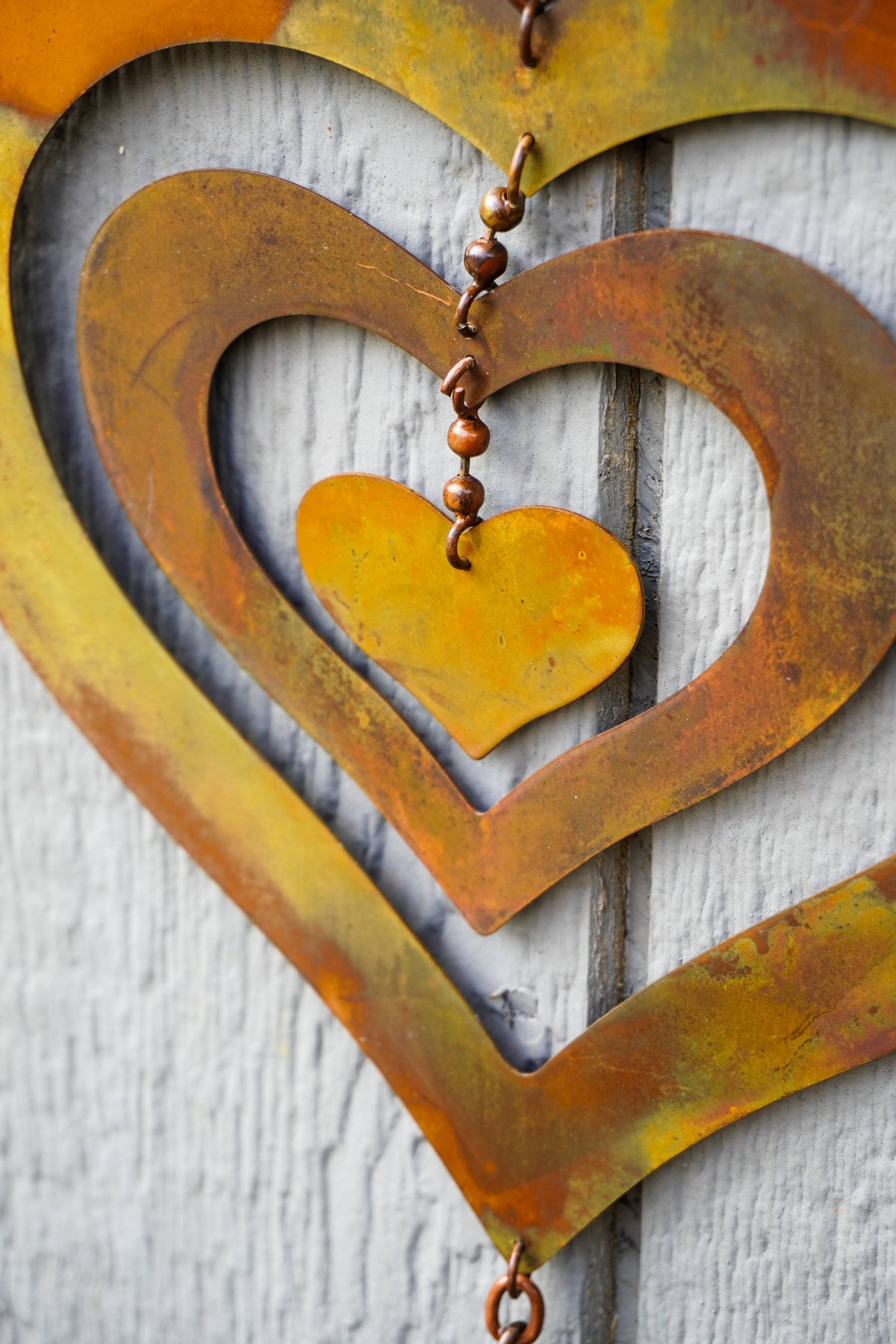 Rustic metal heart wall decor with concentric heart shapes in orange, brown, and gold tones, hanging against a white painted wood background.