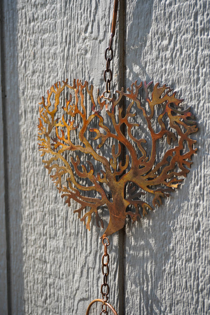 A rusted metal heart-shaped tree ornament hanging from a chain against a textured white wooden door.