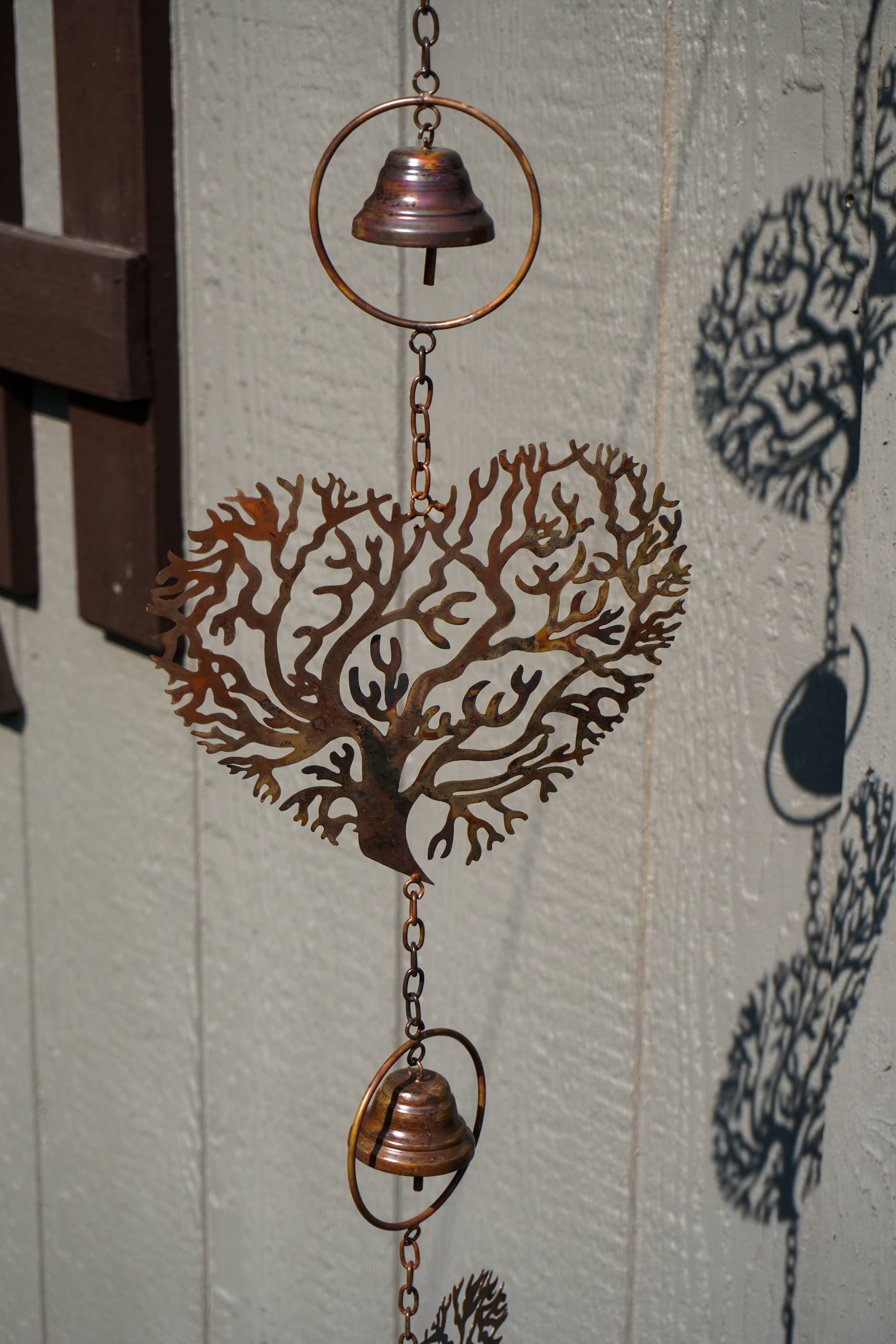 A copper-toned metal wind chime featuring a coral tree design in the center, with two hanging bells and circular rings, shown against a light textured wall.