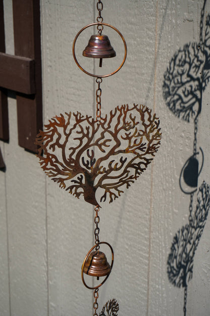 A copper-toned metal wind chime featuring a coral tree design in the center, with two hanging bells and circular rings, shown against a light textured wall.