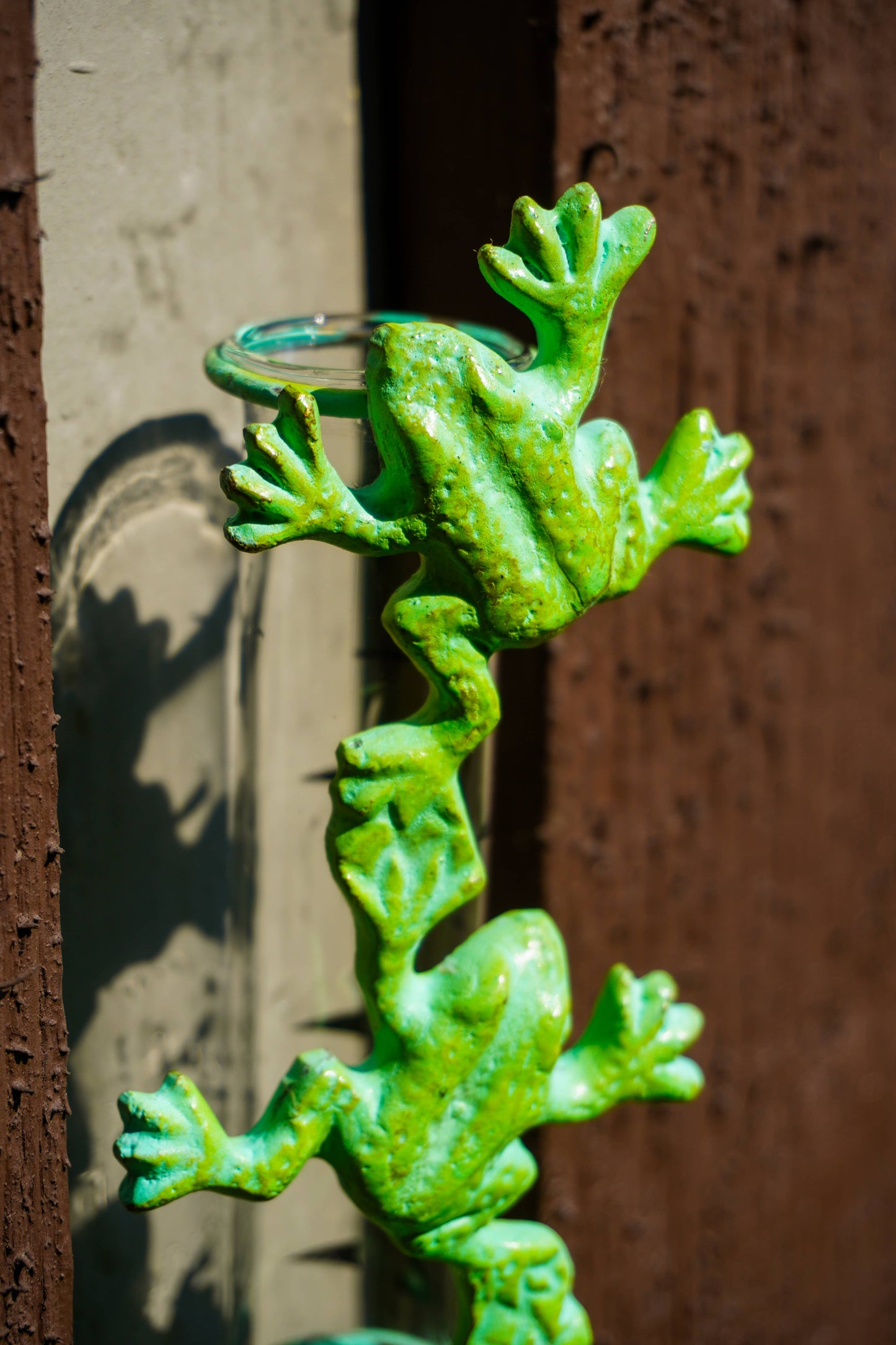 A bright green frog-shaped metal wall decor piece mounted vertically against a textured wall with a brown wooden panel.