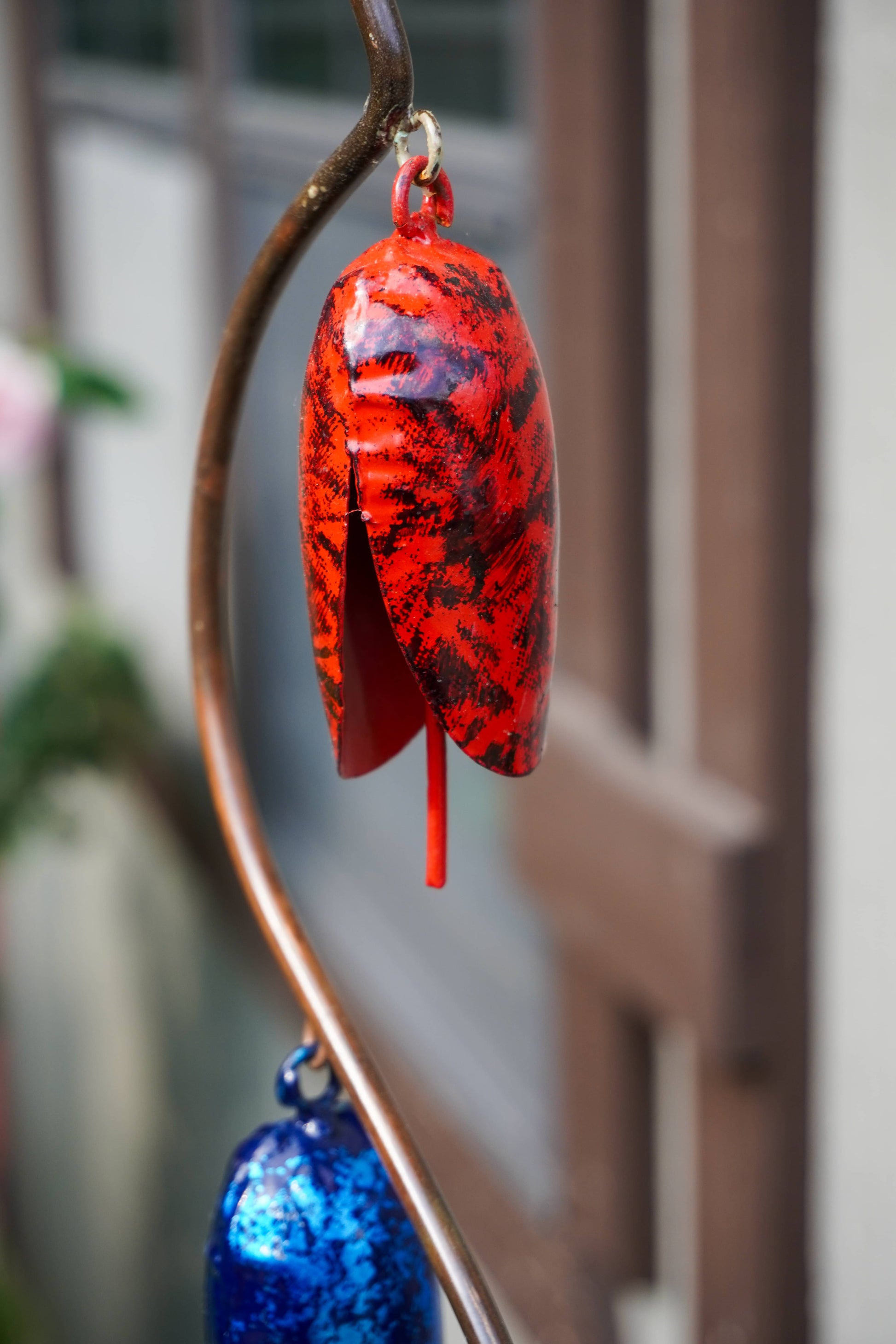 A red and black and blue metal ornament below it, set against a blurred outdoor background.